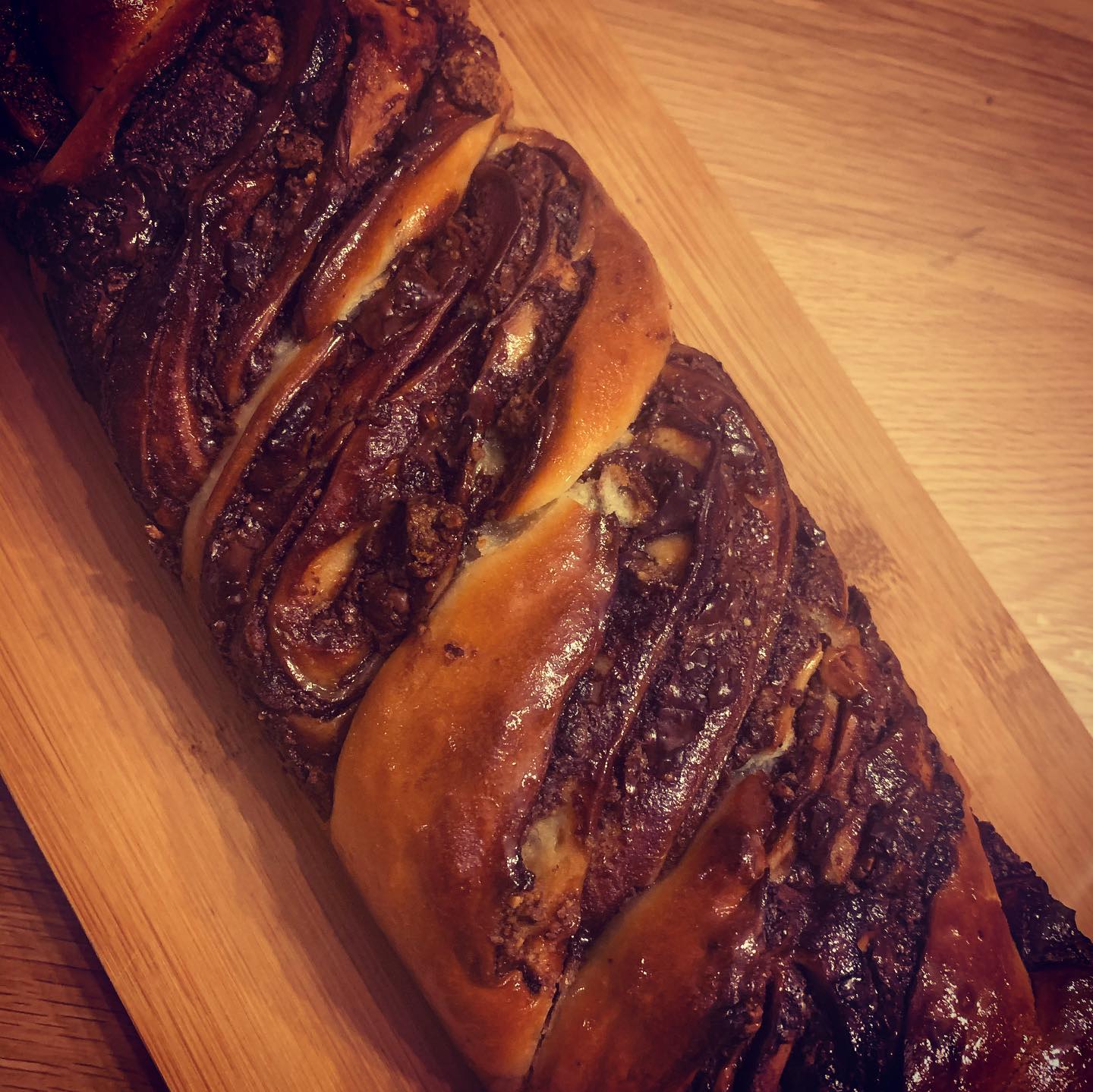 Brioche tressée au chocolat et noix, richement glacée, posée sur une planche en bois clair.
