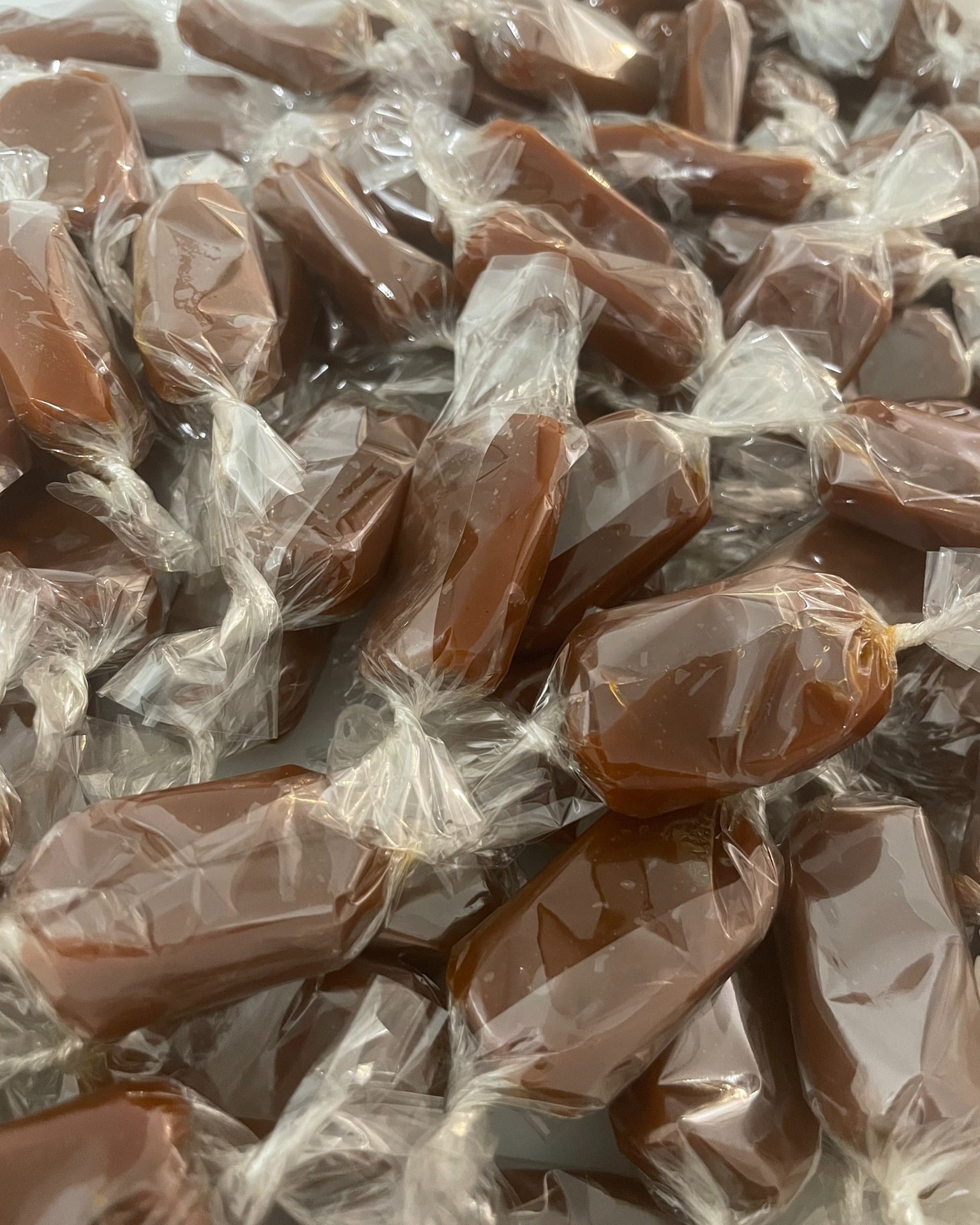 Gros plan sur une grande quantité de caramels individuels emballés dans du plastique transparent brillant, de couleur brun foncé et confiserie.