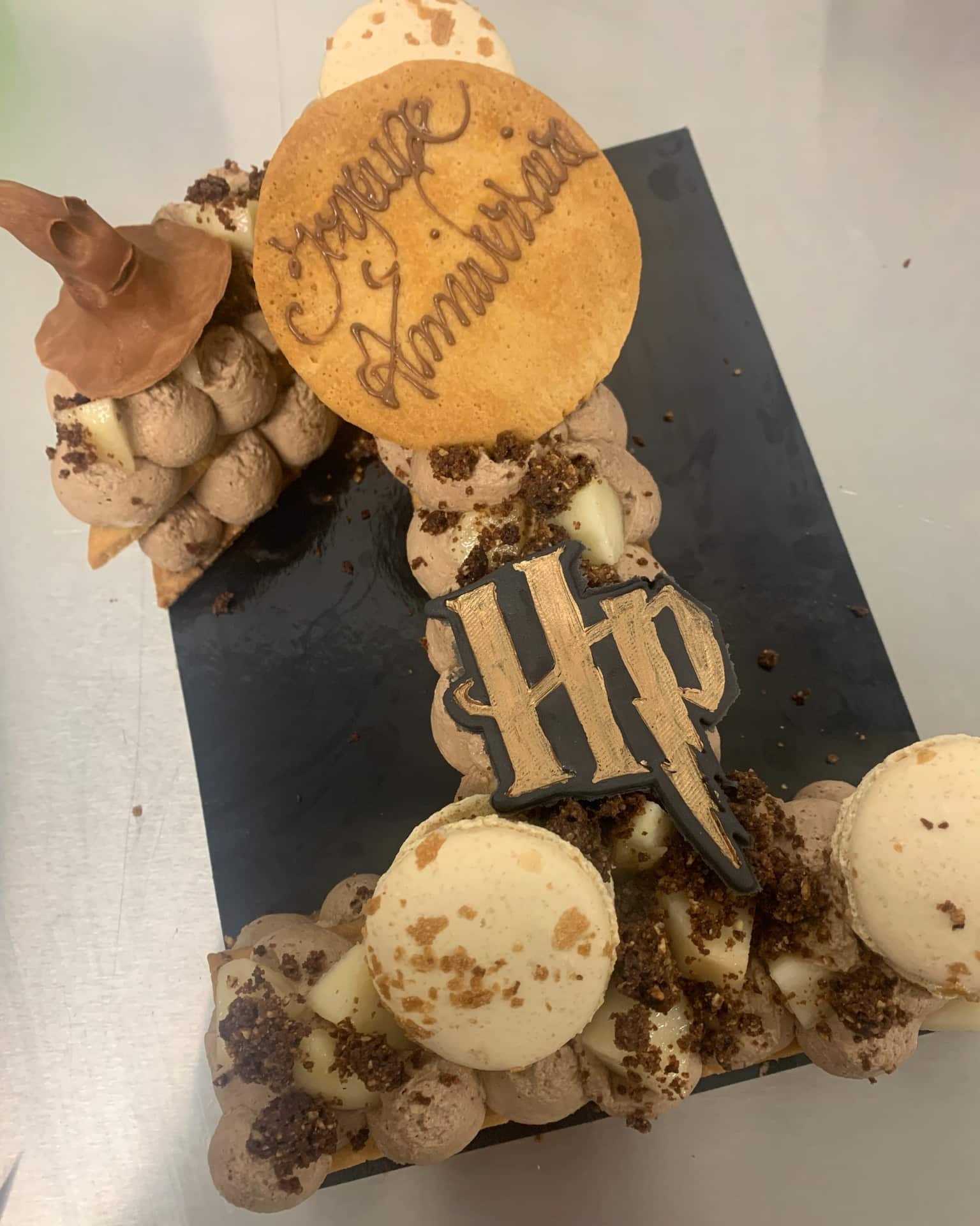 Pâtisserie chiffre 1 Harry Potter avec chapeau de sorcier, cookie "Joyeux Anniversaire", logo HP doré, macarons et crème chocolat.
