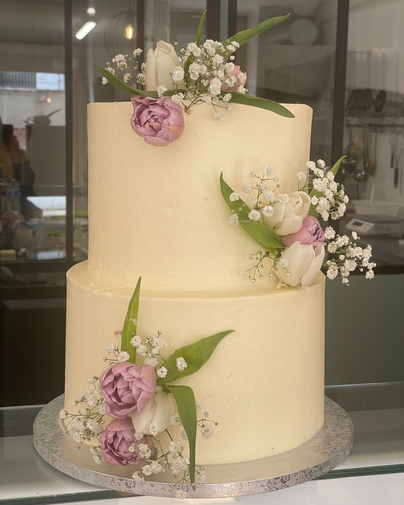 Gâteau deux étages crème avec tulipes violettes et blanches et gypsophile, décoré pour un mariage ou un événement spécial.